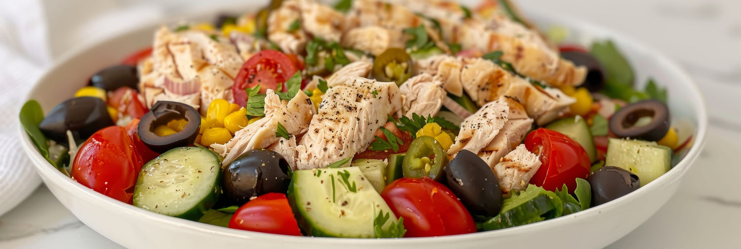 A delicious bowl of chicken salad with olives, cucumber, tomatoes, herbs and other delicacies