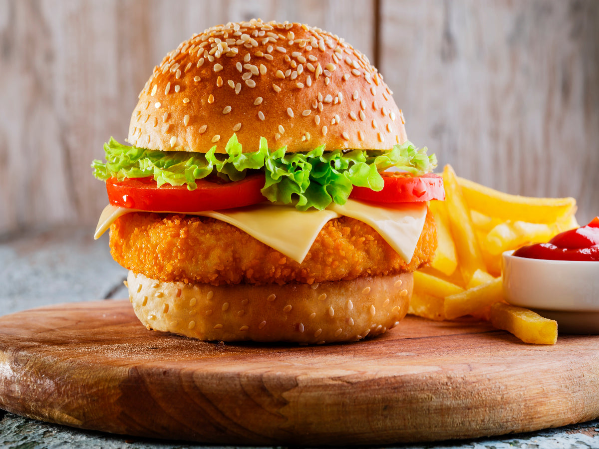 Grilled chicken burger with fresh vegetables, melted cheese, and a soft bun on a wooden cutting board.